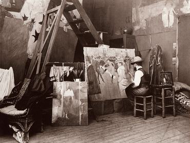 Henri de Tolouse-Lautrec munka közben (1890), műtermében. A festő egy széken ül, mögötte A Moulin ROuge táncosai című félkész festmény