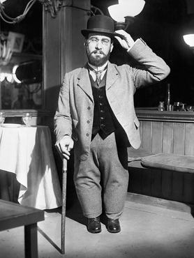 Henri de Toulouse-Lautrec botra támaszkodva, kalapban és öltönyben, kezét kalapjához érintve áll