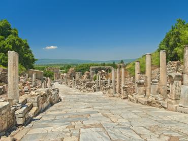 marble alley with columns leading to the Celsus Library in ancient greek city of Ephesus with mountains and clear blue sky at background with single small cloud over the Celsus Library, Turkey