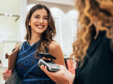 Egy gyönyörű, elegáns nő okostelefonjával fizet egy ruhaüzletben. Egy fiatal nő ruhákat vásárol egy butikban. Egy női vásárló fizet egy luxus divatáruházban.