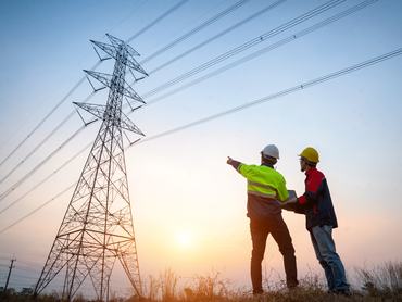 Két szakember egy nagyfeszültségű villanyvezetéket ellenőriz a szabadban