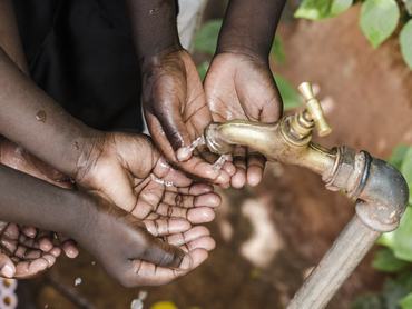 Afrikai gyerekek egy csapból folyó víz alá tartják a kezüket a vízhiány közepette