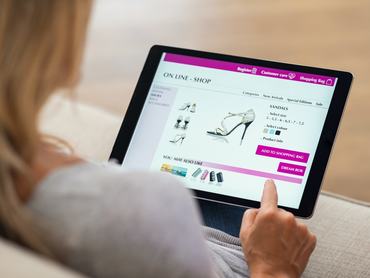 Közelkép egy nőről, aki otthon digitális táblagépen vásárol online. Hátulnézet egy nőről, aki az ujjával megérinti a képernyőt, miközben cipőt választ egy e-kereskedelmi portálon. A hölgy egy e-kereskedelmi webáruházban vásárol cipőt. (Közelkép egy nőről, aki otthon digitális táblagépen vásárol online
