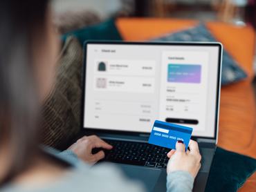 Egy nő váll feletti nézetből látható, ahogy laptopján online ruhákat vásárol, és hitelkártyával fizet. Élvezi a szezonális leárazásokat. „Shopaholic” koncepció. Kiberbiztonsági ötlet. Közelkép. Laptop-képernyő makett.
